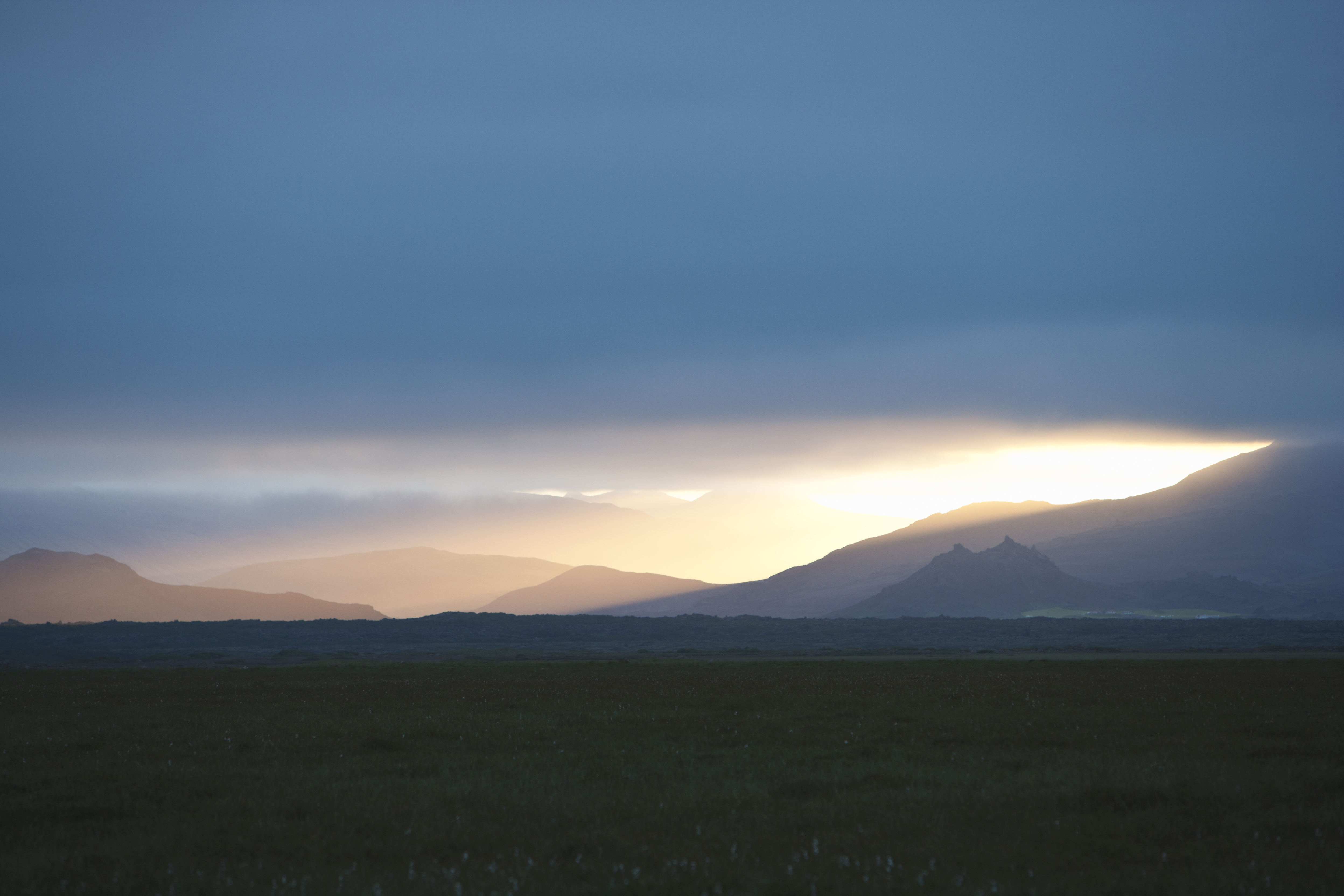 Sunlight coming through the clouds over a landscape of mountains and fields, Iceland.